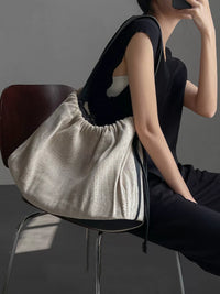 Person sitting on a chair with a large beige drawstring bag on their lap against a gray background