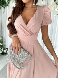 Woman in a pink dress holding a silver clutch against a white background