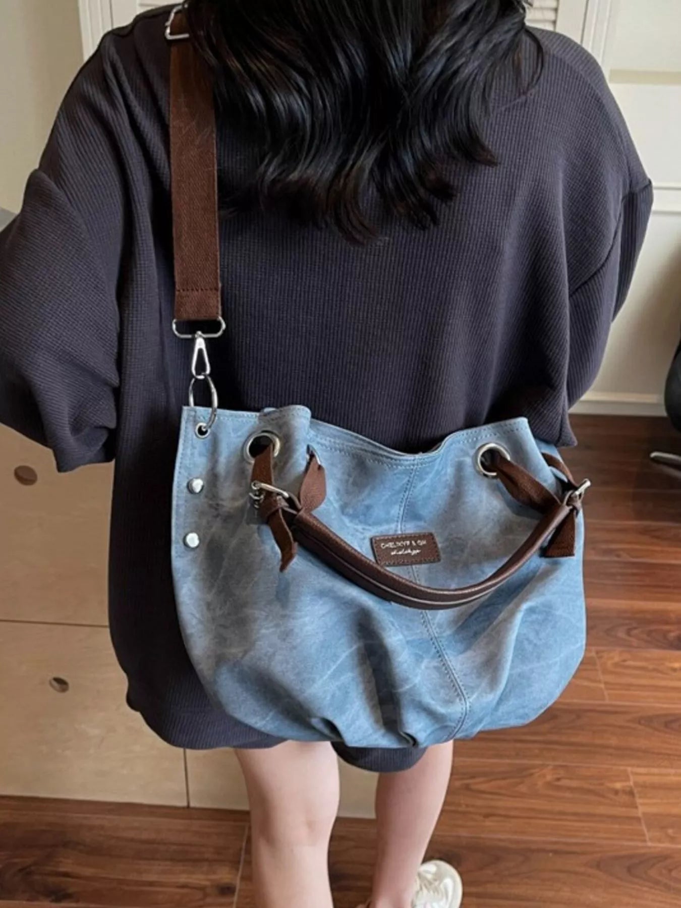 Person holding a blue handbag with brown straps indoors