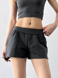 Person wearing black shorts and a gray crop top on a plain background