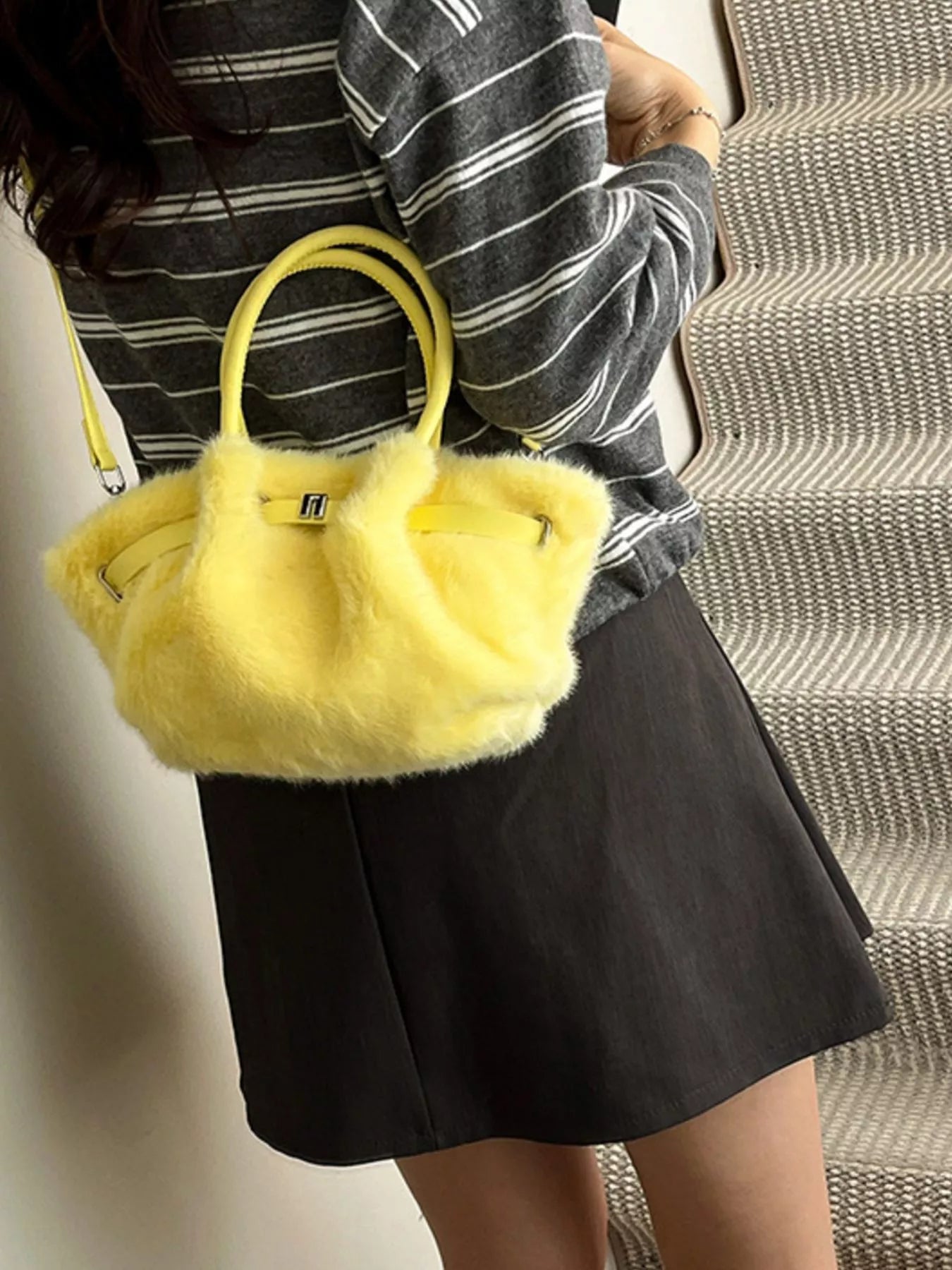 Person holding a yellow fluffy handbag with a striped shirt and black skirt.