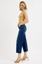 Woman wearing a mustard yellow top and blue jeans on a white background