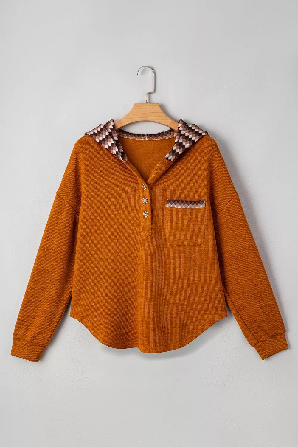 Brown shirt with patterned collar and pocket on a hanger against a gray background