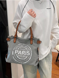 Person holding a gray tote bag with 'Paris' text, wearing a white sweatshirt and light pants.