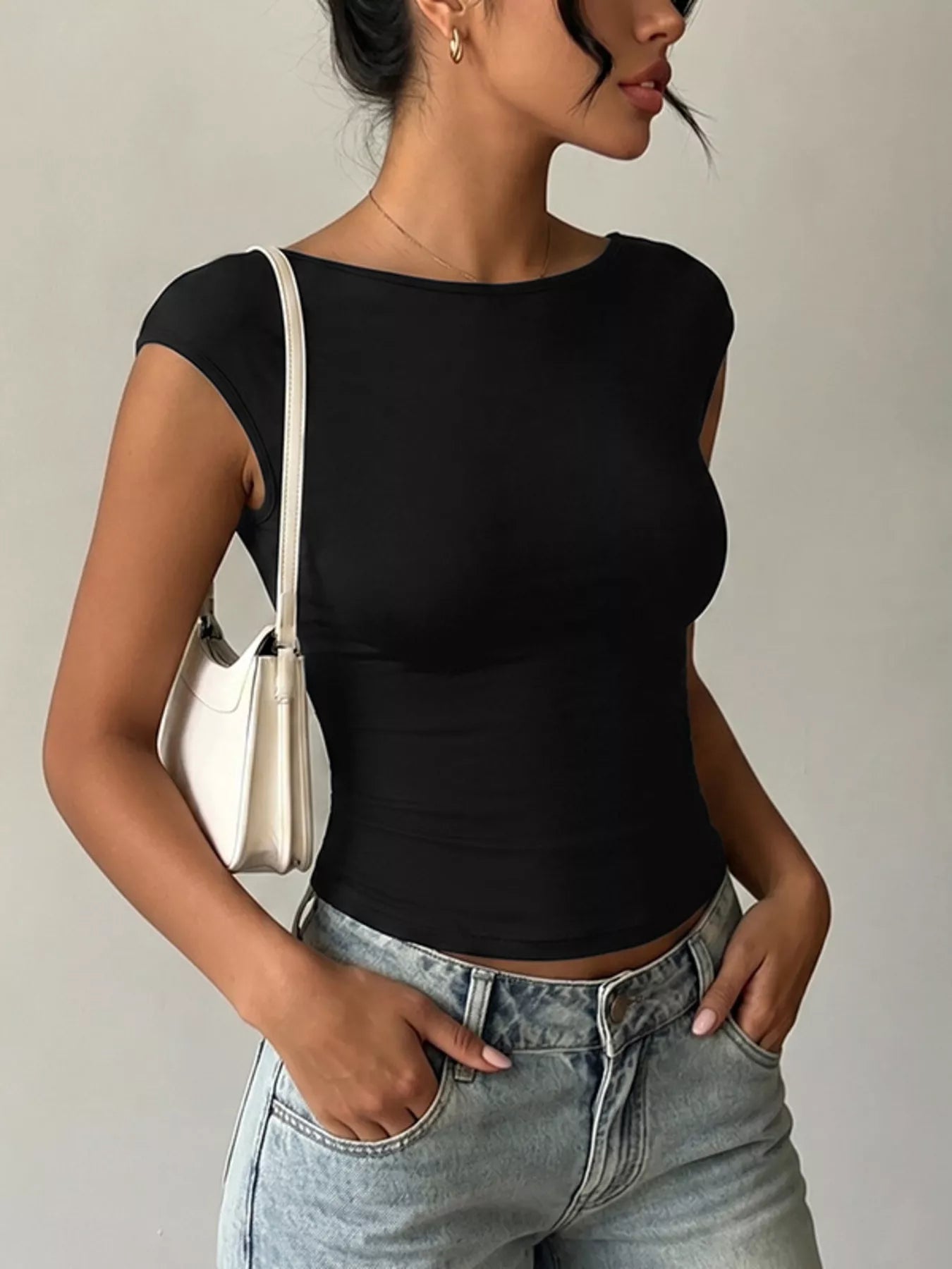 Woman wearing a black top and light blue jeans with a neutral background