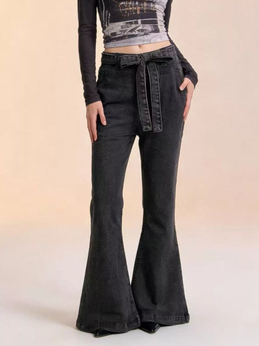 Black bell-bottom pants worn by a person on a beige background