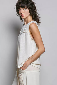 Woman wearing a sleeveless white top with lace details against a plain background