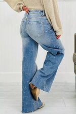 Person wearing blue flared jeans and a beige sweater on a white background