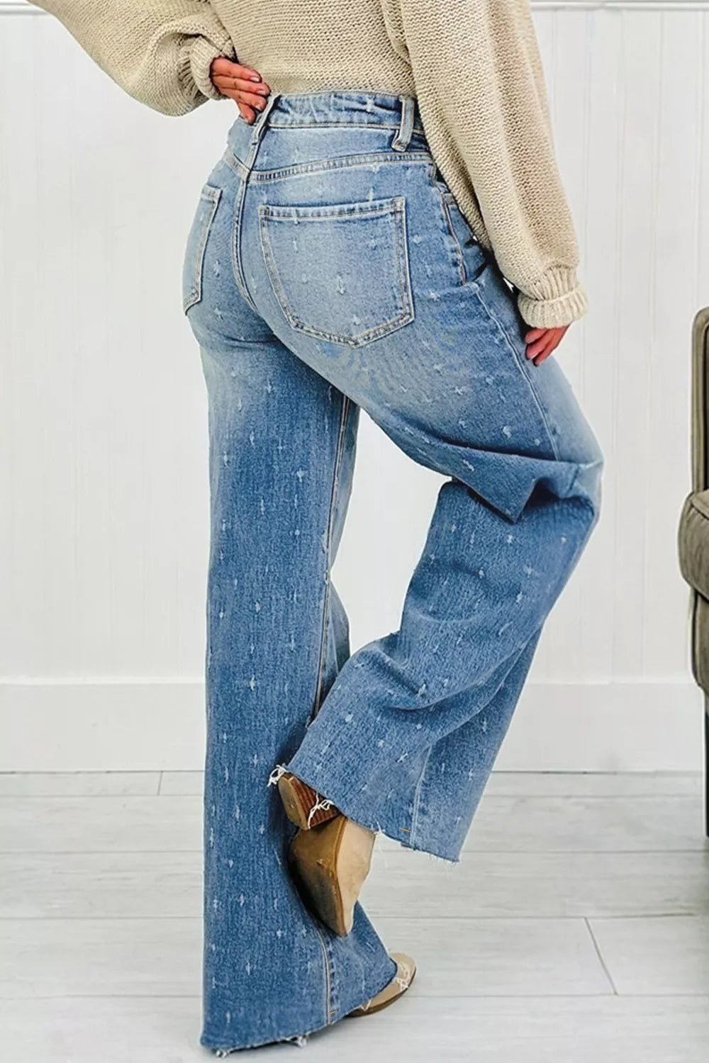 Person wearing blue flared jeans and a beige sweater on a white background