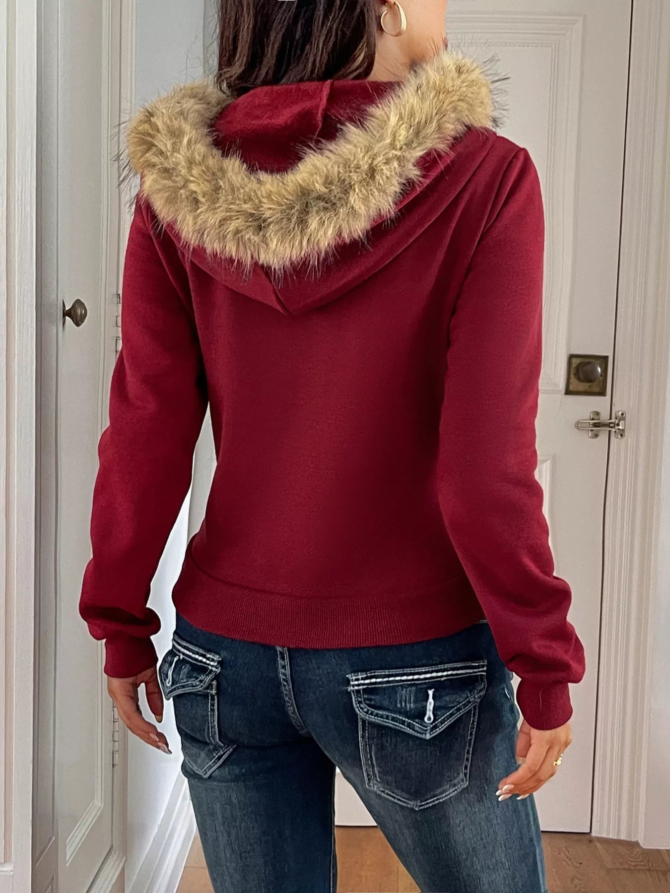 Red hoodie with fur-lined hood worn by a person, standing in a room.