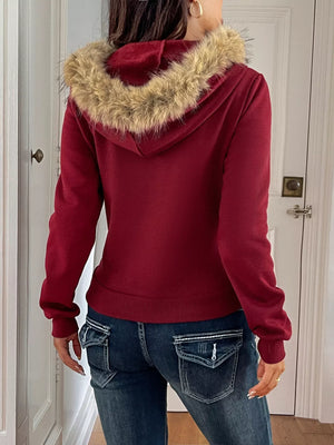 Red hoodie with fur-lined hood worn by a person, standing in a room.