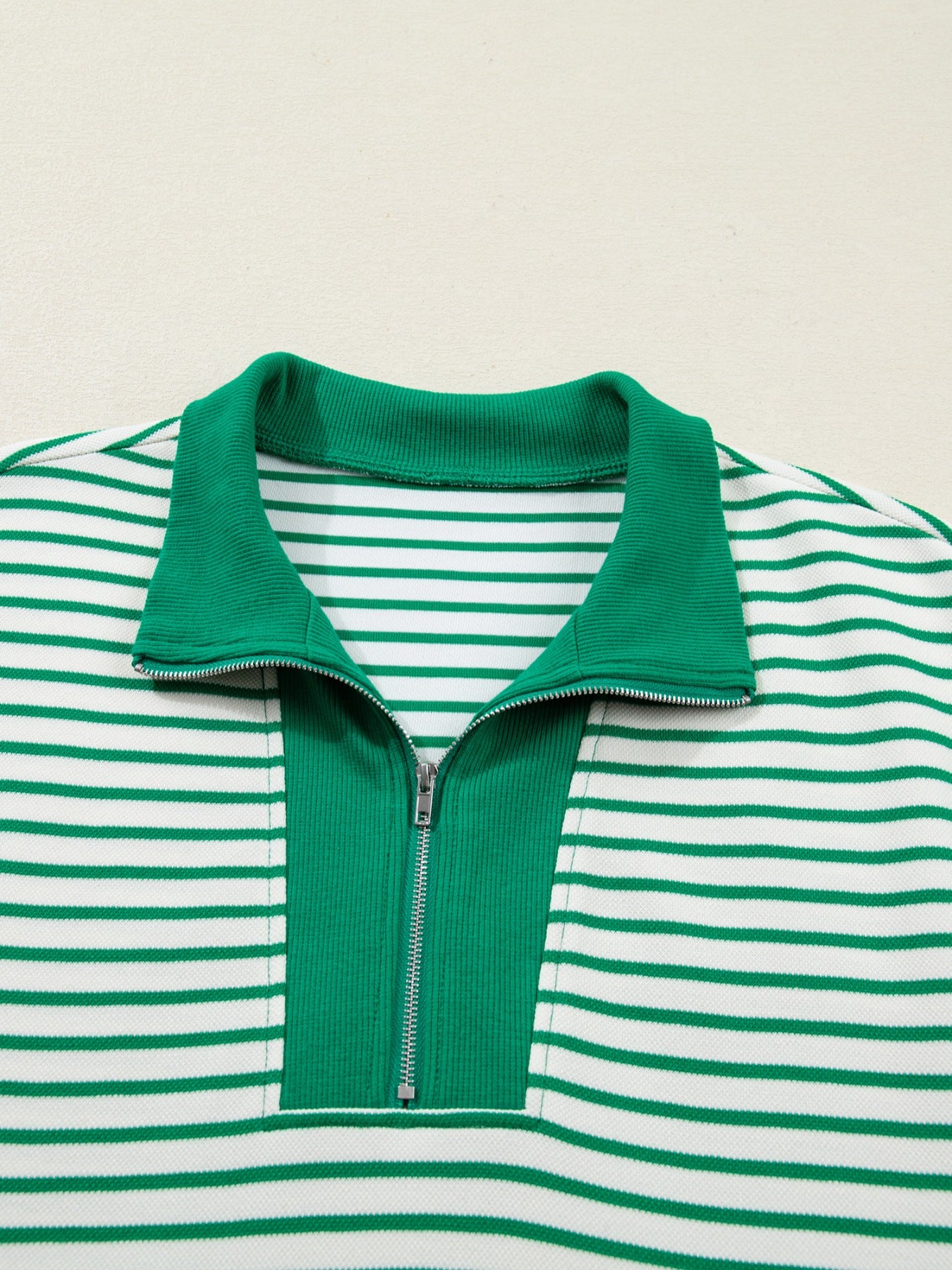 Green and white striped shirt with a collar and zipper on a beige background