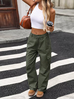 Person wearing green cargo pants and a white top, holding a brown handbag and a coffee cup on a street.
