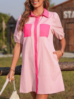 Woman wearing a pink and white striped dress with a wooden structure and greenery in the background