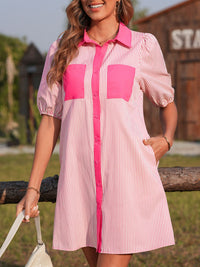 Woman wearing a pink and white striped dress with a wooden structure and greenery in the background