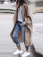 Person wearing a beige coat, light blue jeans, and white sneakers on a blurred street background