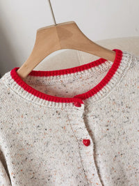 White knitted sweater with red trim on a wooden hanger against a neutral background