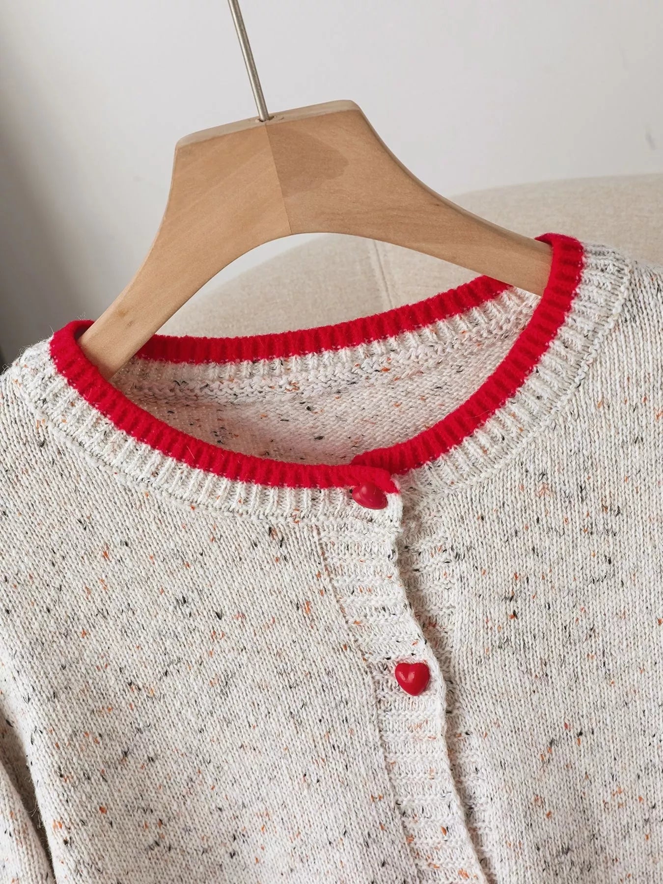 White knitted sweater with red trim on a wooden hanger against a neutral background
