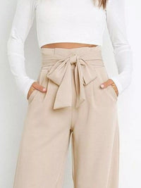 Beige paperbag pants with a tie detail worn by a person on a plain background