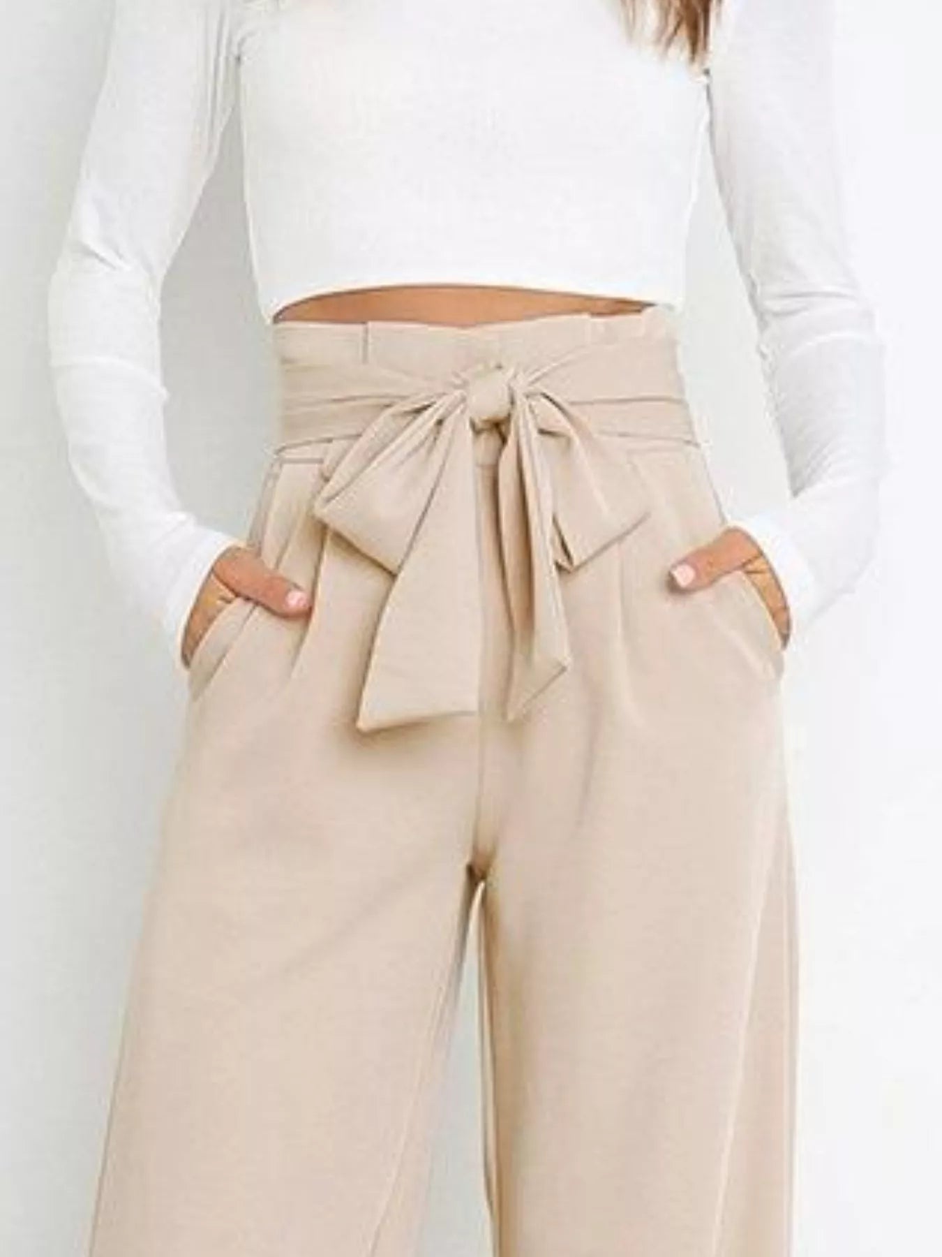 Beige paperbag pants with a tie detail worn by a person on a plain background
