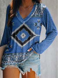 Person wearing a blue patterned long-sleeve top and denim shorts against a neutral background