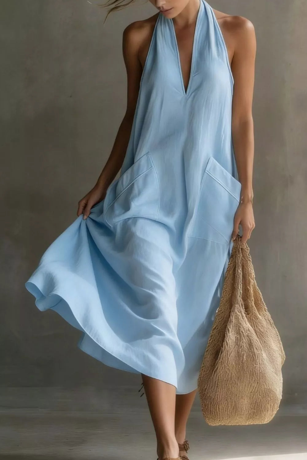Woman wearing a light blue dress holding a brown bag against a neutral background