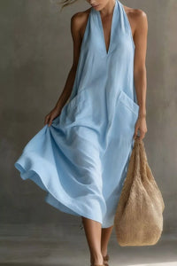 Woman wearing a light blue dress holding a brown bag against a neutral background
