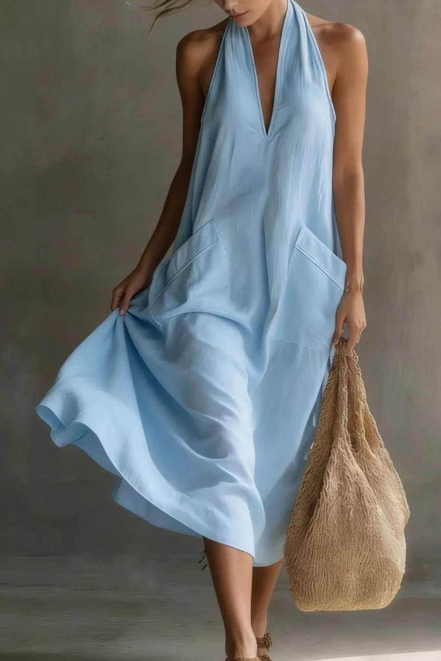 Woman wearing a light blue dress holding a brown bag against a neutral background