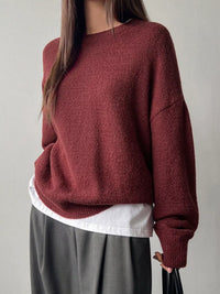 Person wearing a maroon sweater over a white shirt with gray pants on a plain background