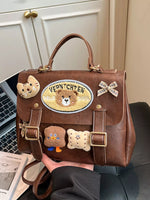 Brown handbag with decorative patches held by a person, with a laptop and newspaper in the background.