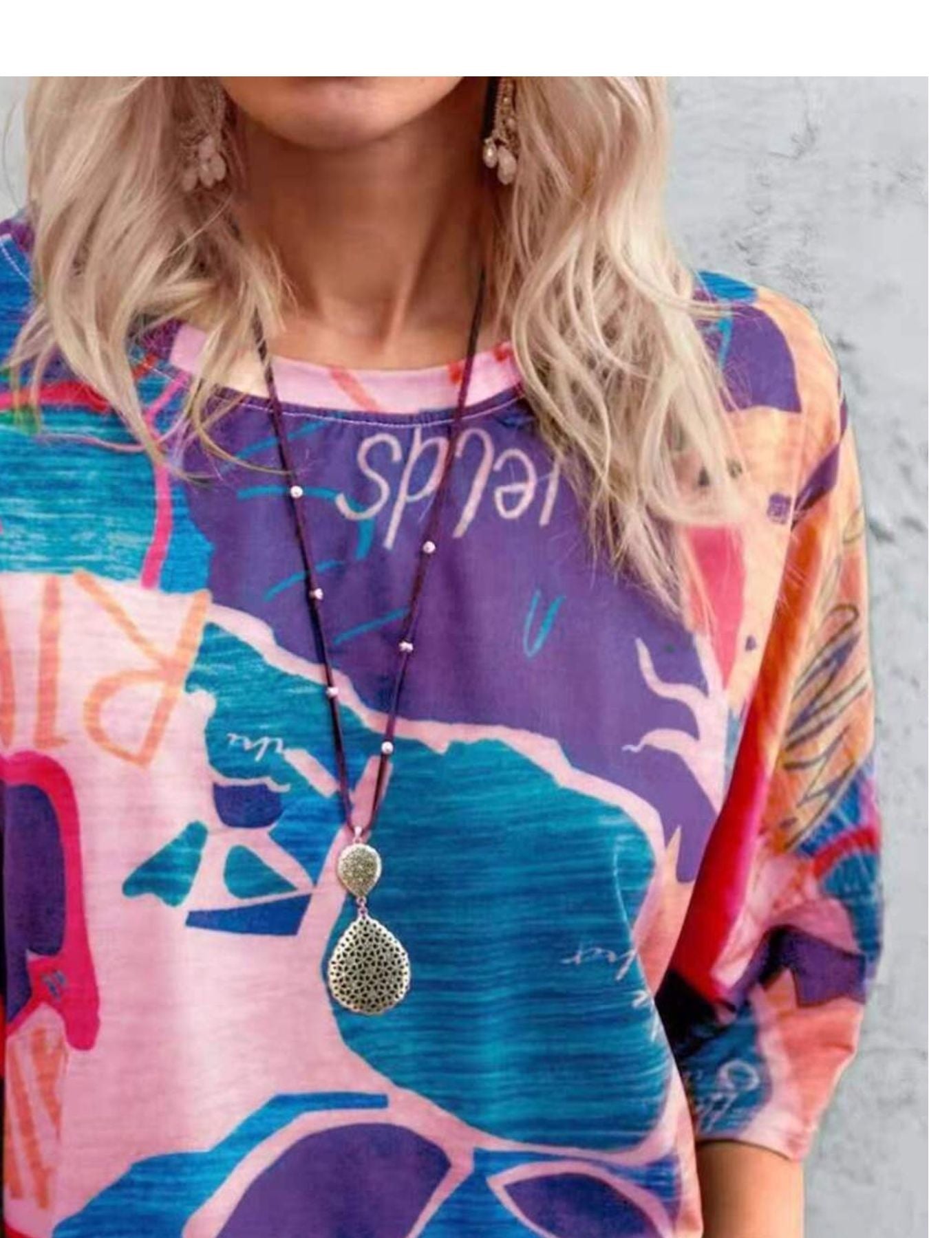 Person wearing a colorful shirt with abstract designs and a necklace.