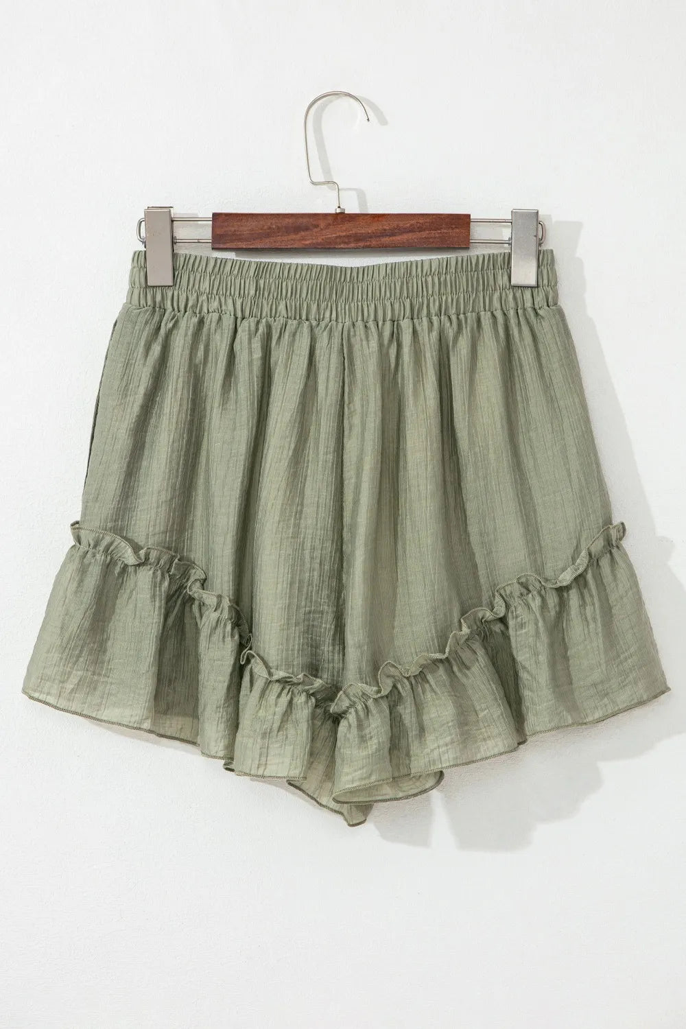Green ruffled shorts on a hanger against a white background