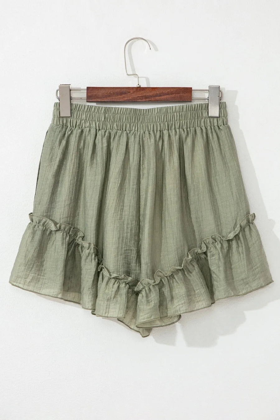 Green ruffled shorts on a hanger against a white background