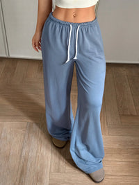 Person wearing blue sweatpants with a white drawstring on a wooden floor.