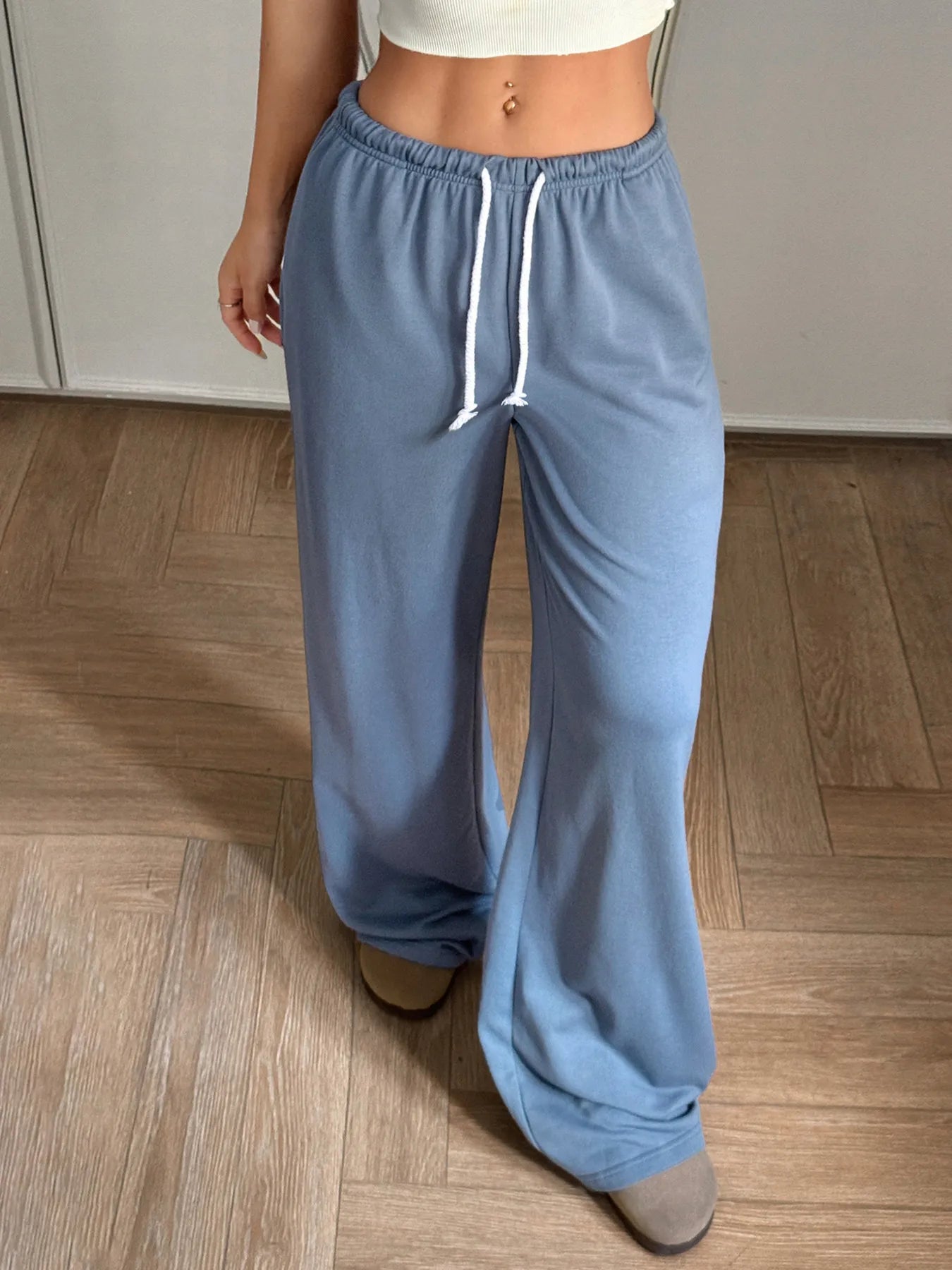 Person wearing blue sweatpants with a white drawstring on a wooden floor.