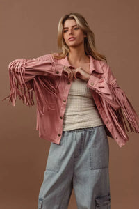 Woman wearing a pink fringed jacket, beige sweater, and blue jeans against a brown background