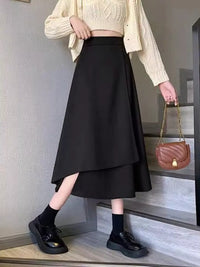 Person wearing a black skirt and beige sweater, holding a brown handbag on a staircase.
