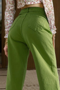 Green pants worn by a person with a floral top, standing against a wooden door.