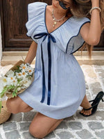 Woman wearing a blue and white striped dress with a bow, sitting on a stone floor.