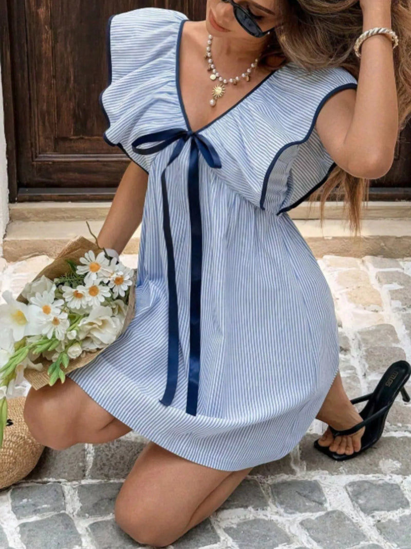Woman wearing a blue and white striped dress with a bow, sitting on a stone floor.
