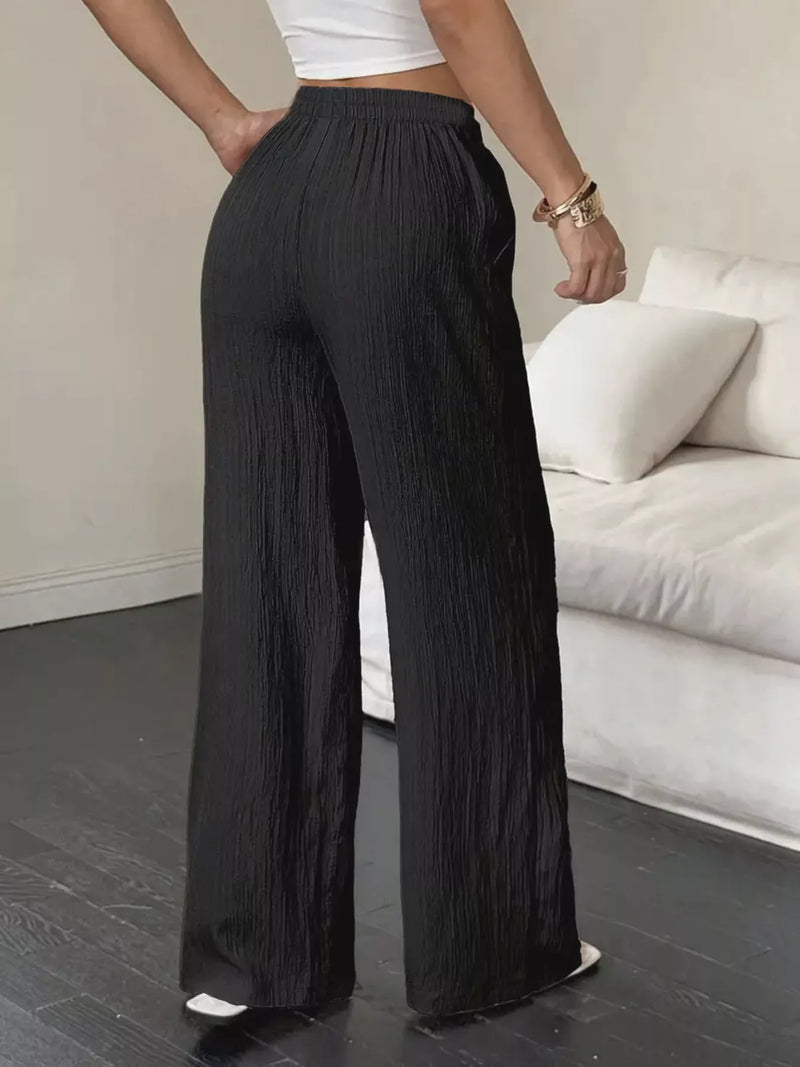 Person wearing black wide-leg pants in a minimal indoor setting