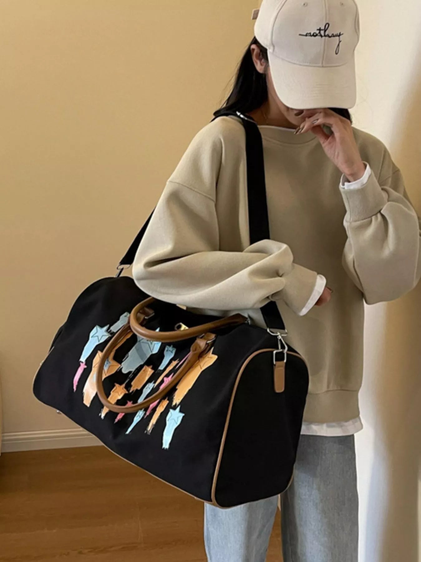 Person holding a black duffel bag with colorful handles against a beige wall.