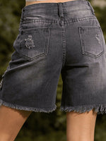 Black denim shorts with frayed edges on a blurred natural background
