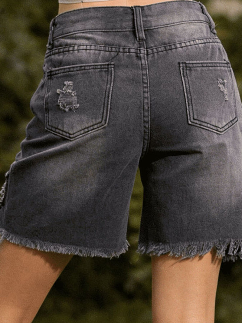 Black denim shorts with frayed edges on a blurred natural background