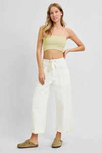 Woman wearing a light green crop top and white pants on a plain background
