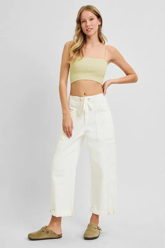 Woman wearing a light green crop top and white pants on a plain background