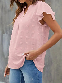 Woman wearing a pink blouse with ruffled sleeves and blue jeans against a gray background