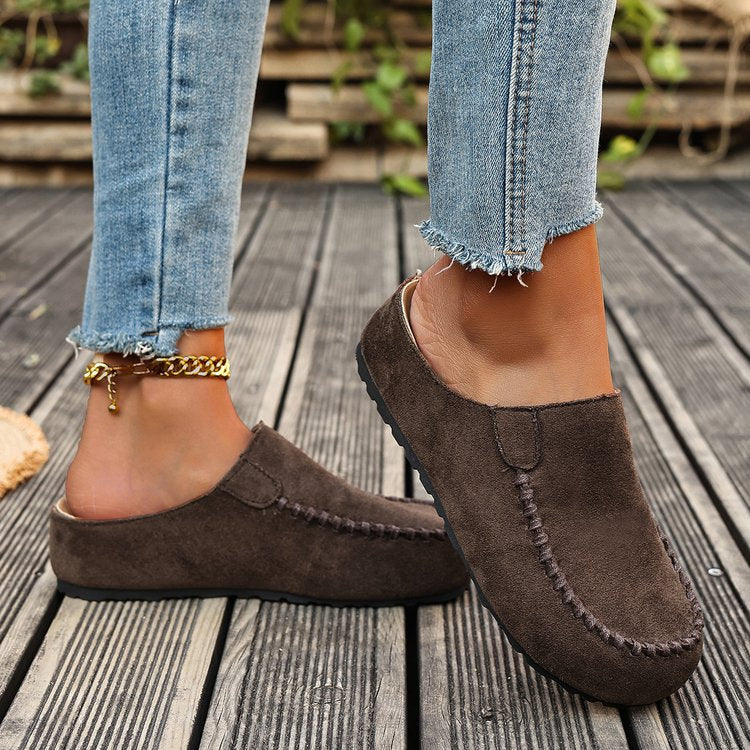 Brown suede loafers worn with light blue jeans on a wooden deck.
