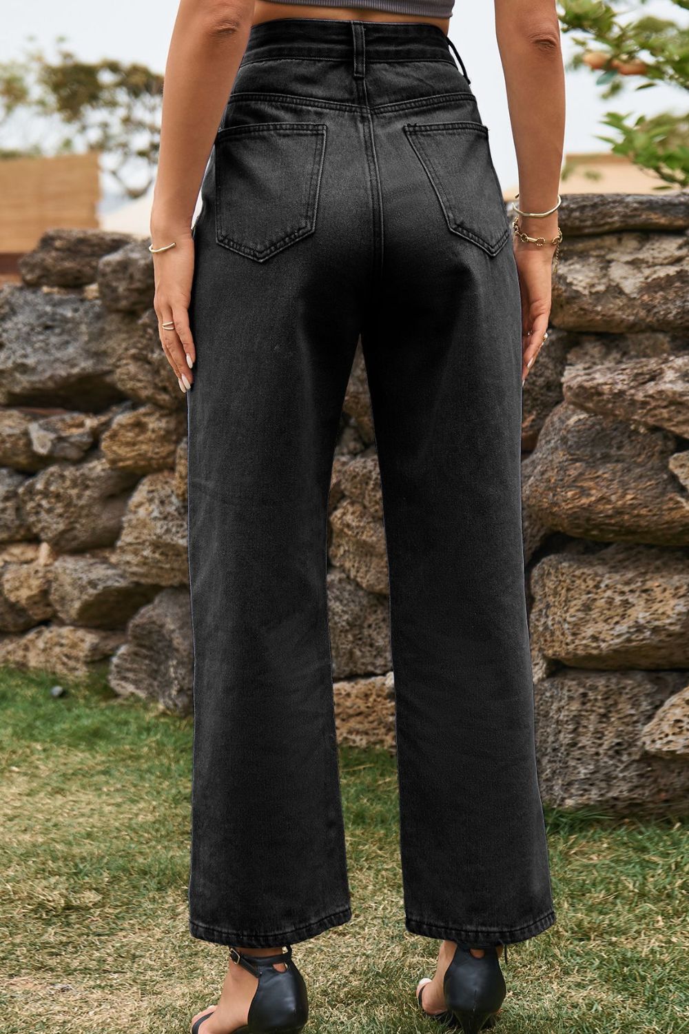 Person wearing black wide-leg jeans standing in front of a stone wall.