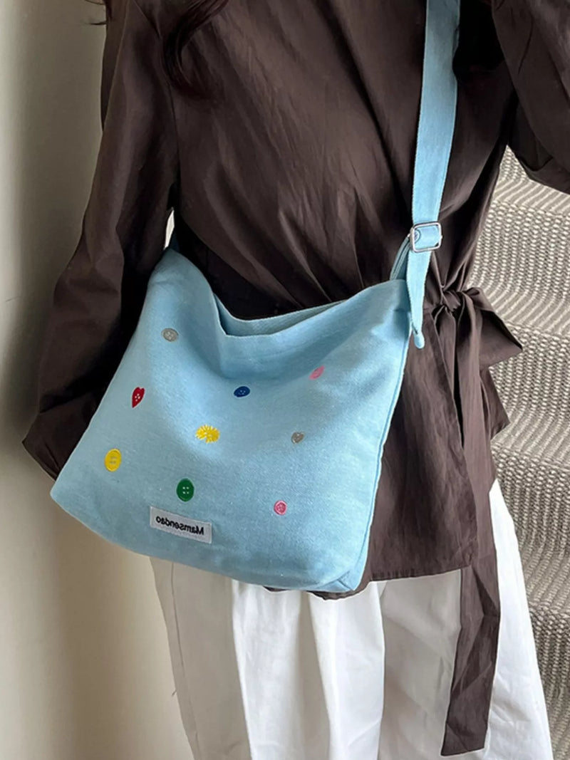 Light blue shoulder bag with colorful polka dots worn by a person in a brown shirt and white pants.